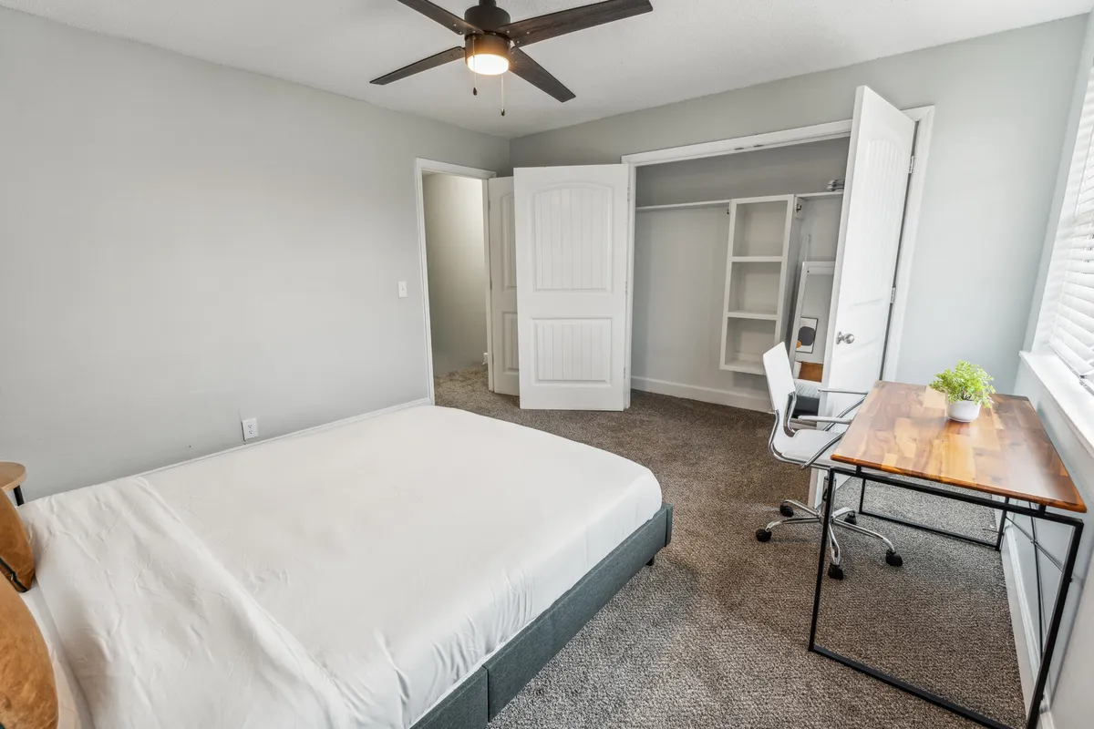 A cozy multi-purpose bedroom with a bed, an open closet, and a tidy desk area, perfect for studying, working remotely, or enjoying a quiet evening with a book. Soft lighting and uncluttered décor create a relaxed and productive mood.
