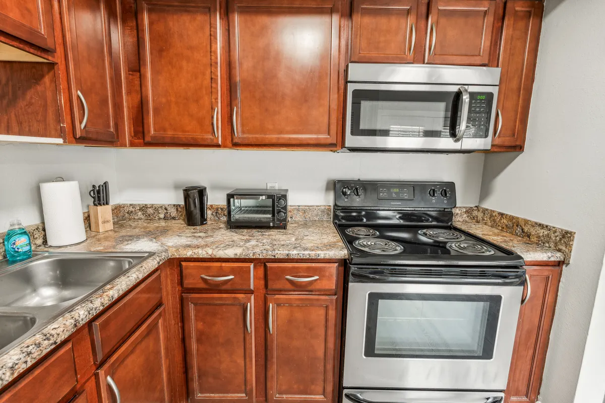 This image showcases a spacious kitchen with inviting warm tones. Granite countertops are paired with modern stainless steel appliances and well-organized kitchen cabinets. The kitchen looks fully equipped for cooking and entertaining, with ample counter space and a sink positioned for convenience. The overall layout is warm and functional, ideal for everything from daily meals to special gatherings.