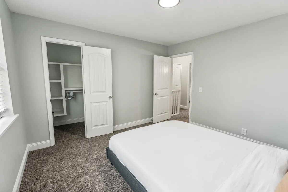 A tranquil bedroom with a cozy bed positioned near doorways, flooded with natural light from a window. The ambiance is calm, with soft tones that invite relaxation and privacy.