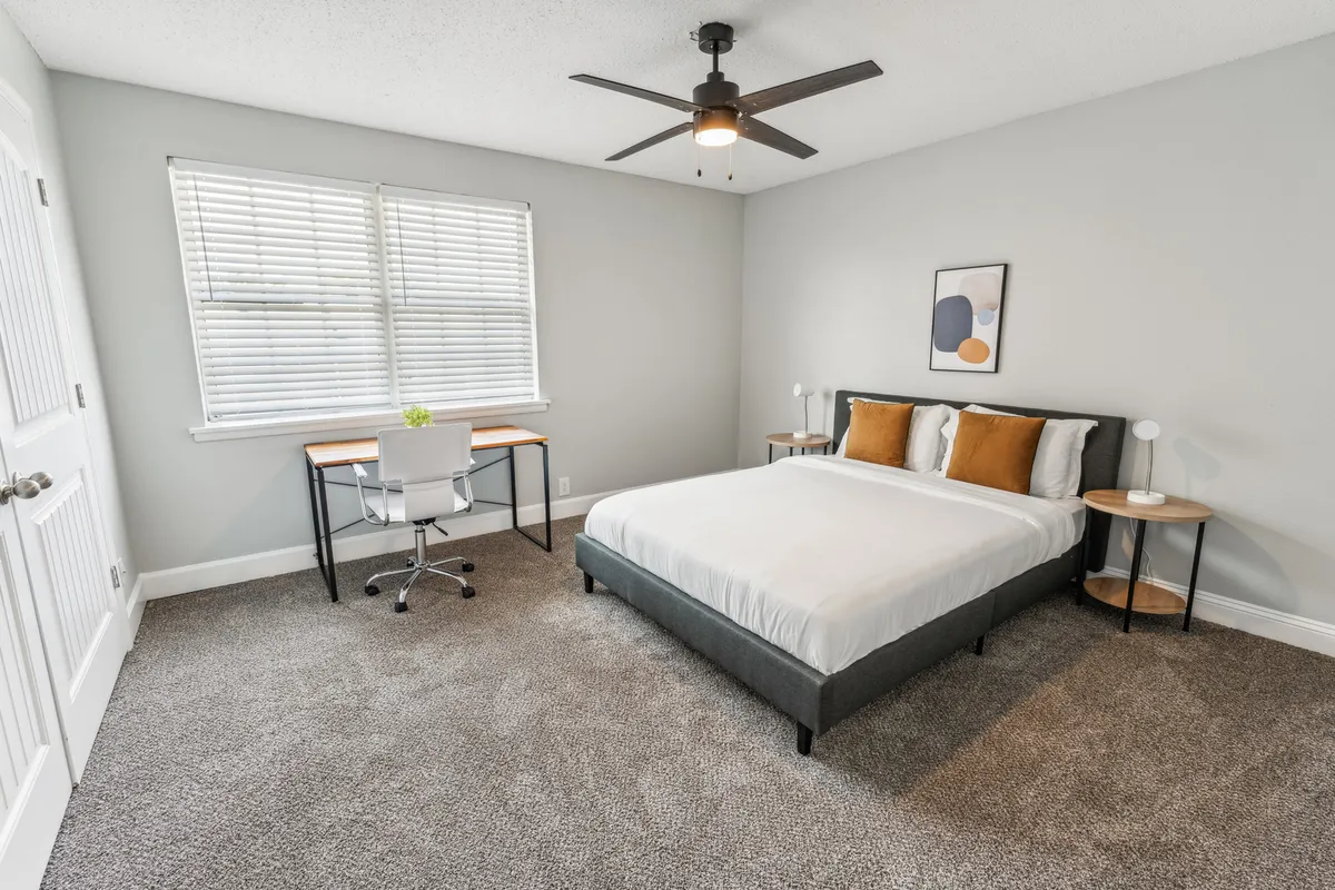 A bright, inviting bedroom with a comfortable bed, a small desk by the window, and cheerful artwork on the wall. Sunlight pours through the window, creating a peaceful, relaxed atmosphere ideal for unwinding after a day out.